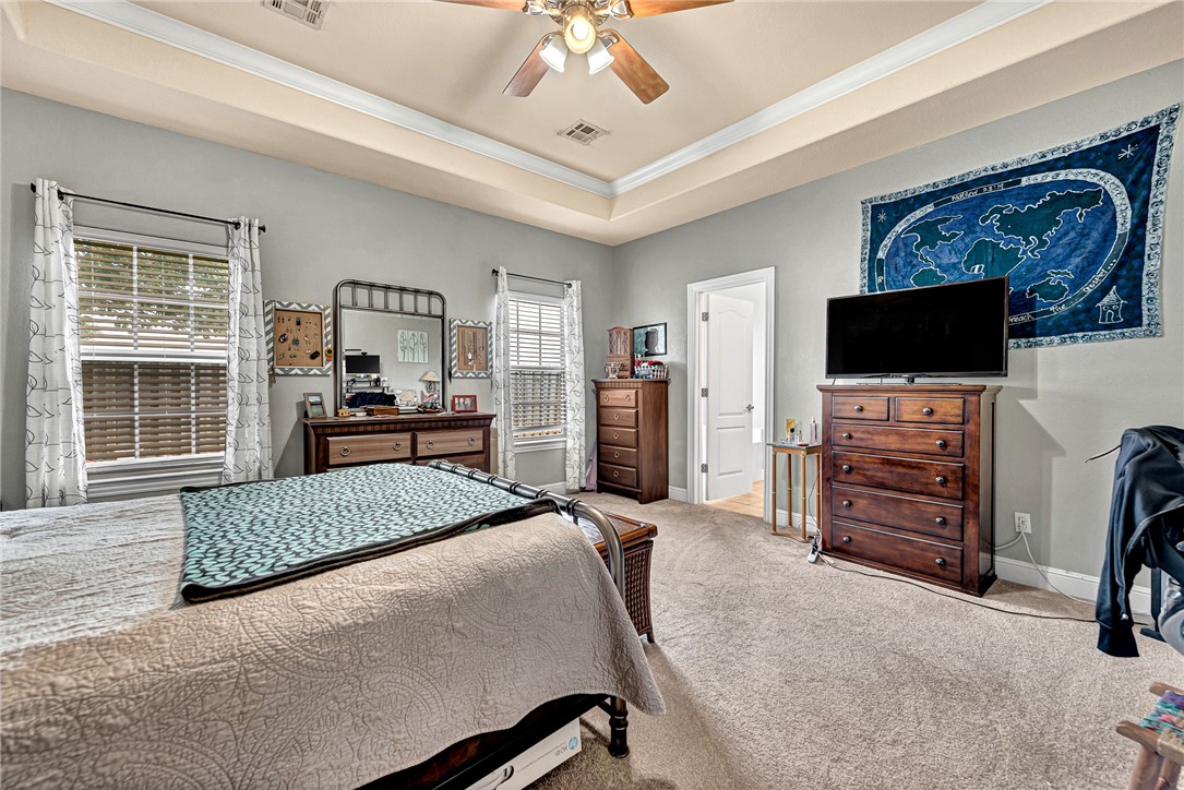 Bedroom with a large bed, tray ceiling, ceiling fan, and television above a dresser.