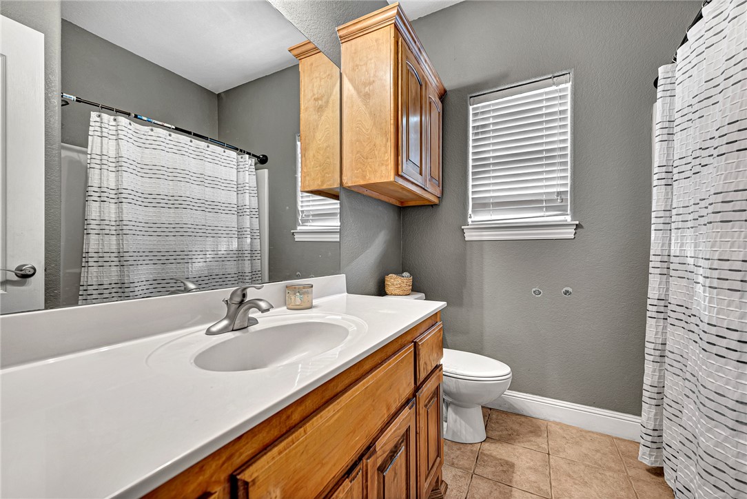 Bathroom with a long white vanity, wooden cabinets, and a toilet beside a tiled shower.