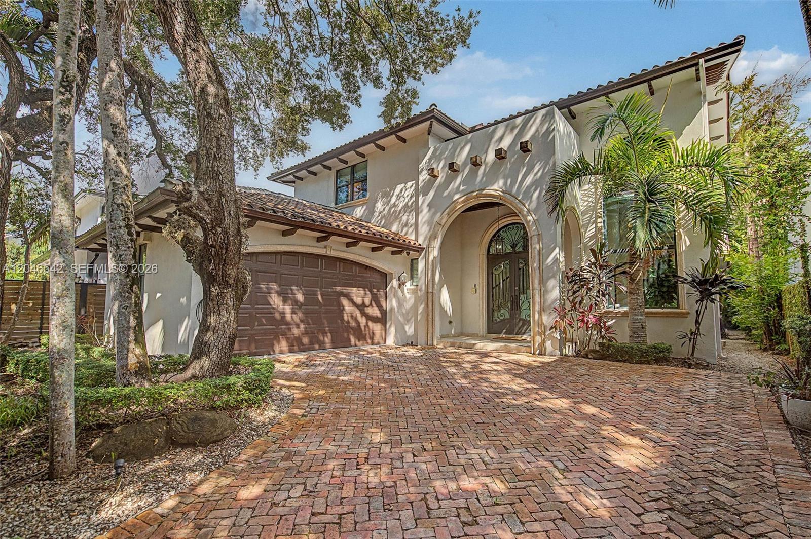 Two-story stucco home with an arched entry, tile roof, and brick-paved driveway.