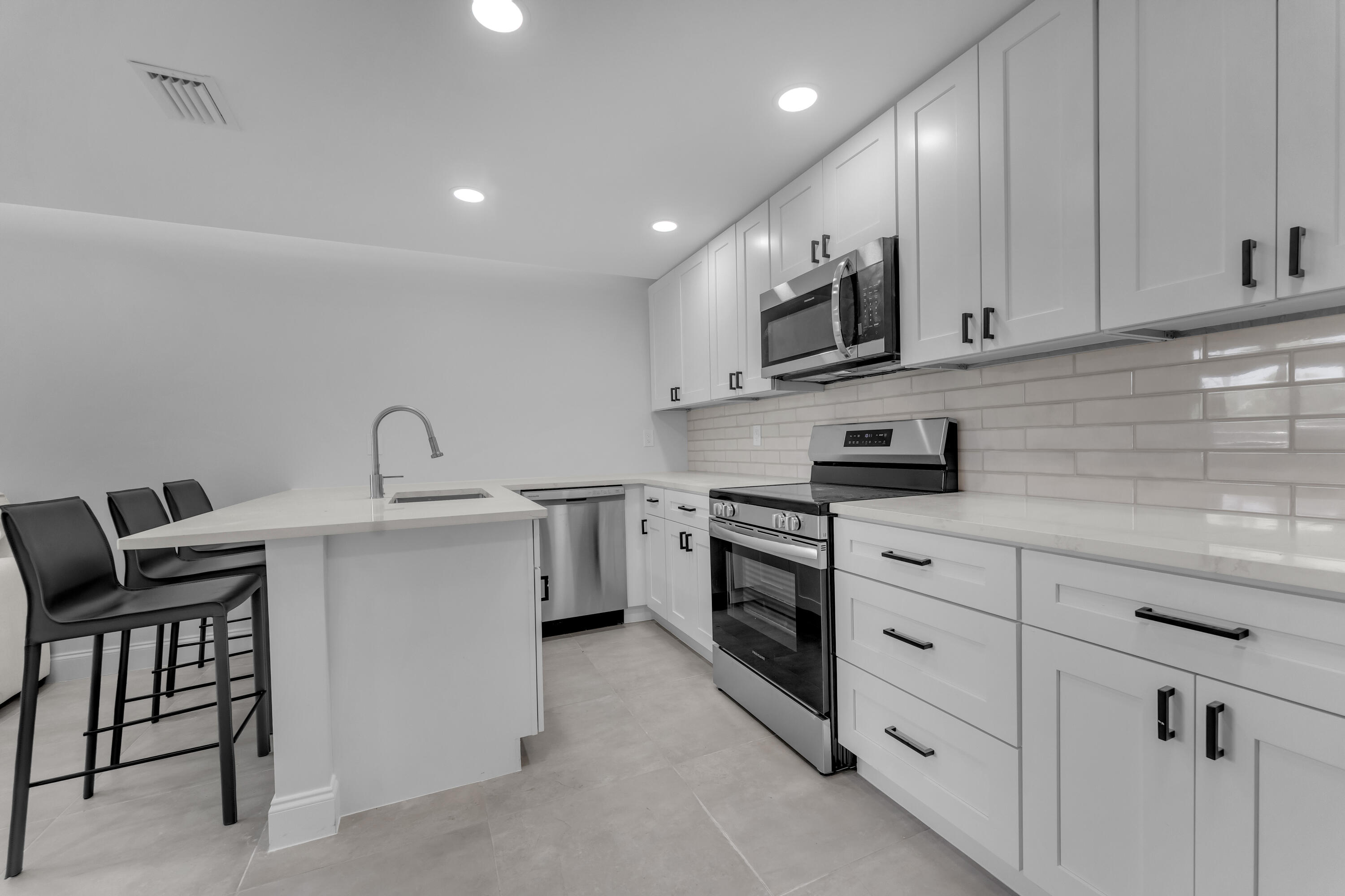Modern kitchen with white cabinets, stainless steel appliances, and an island with a sink and bar stools.