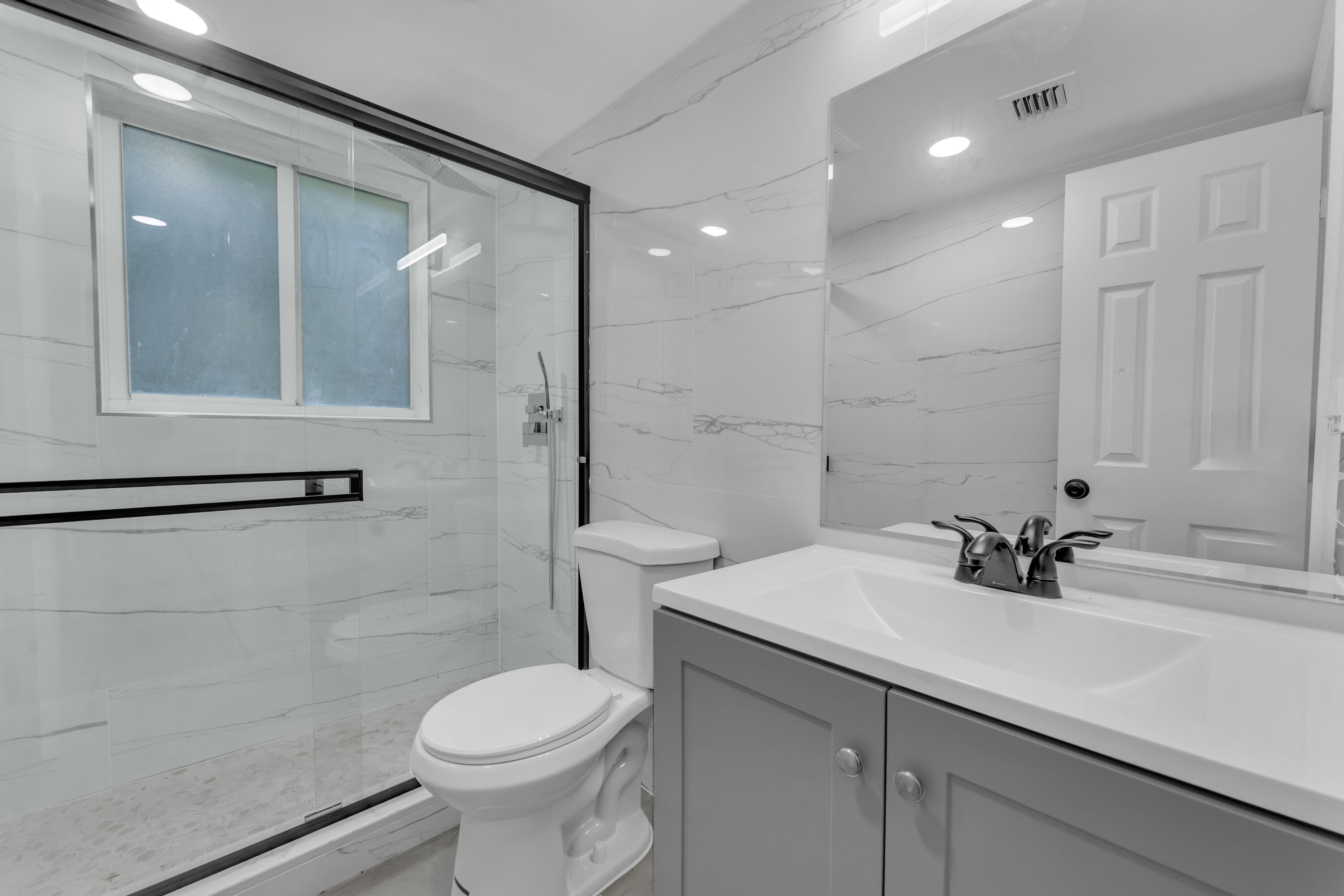 Renovated bathroom with a glass shower, marble-look tile, and gray vanity.