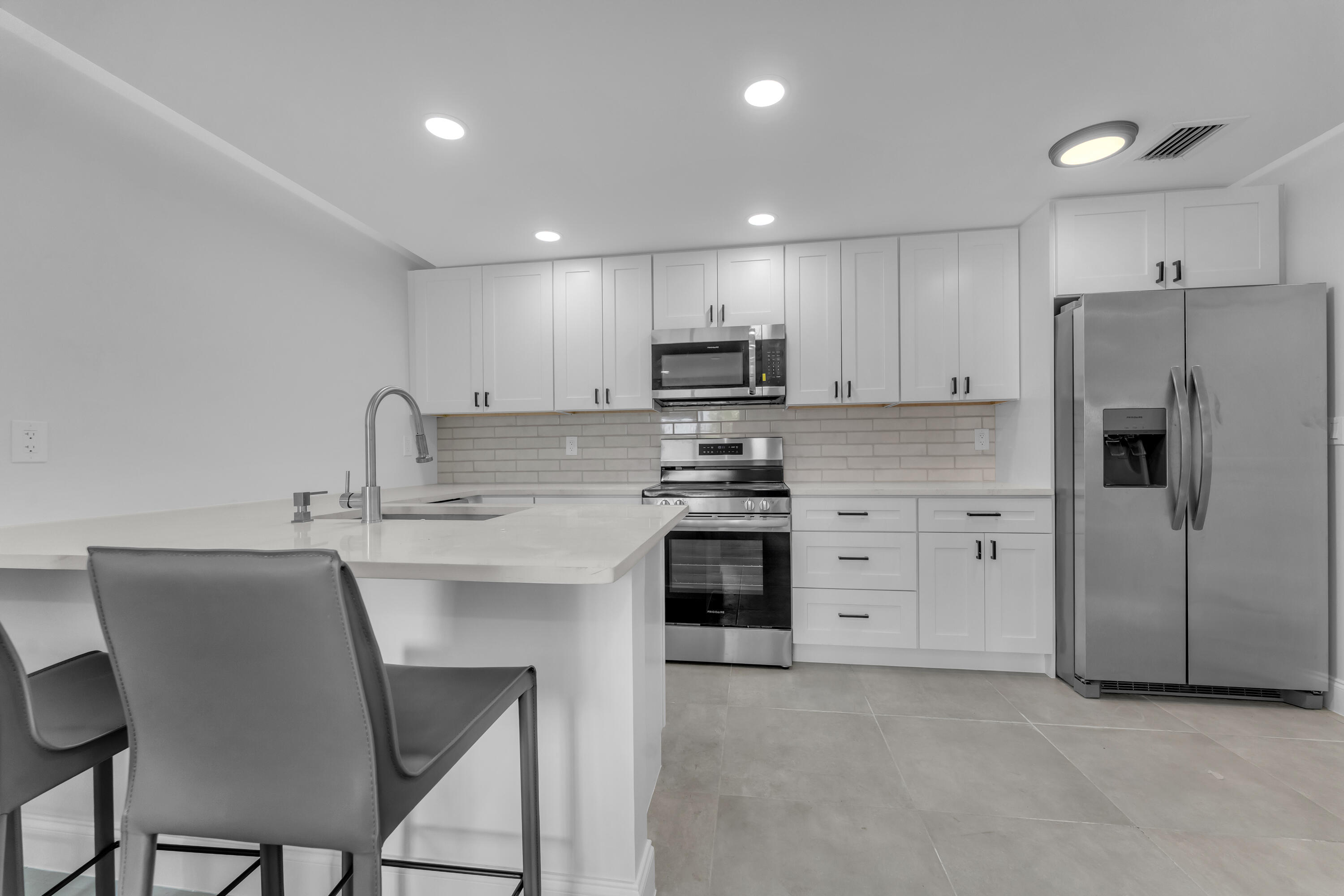 Modern kitchen with white cabinets, a large island, stainless steel appliances, and gray bar stools.