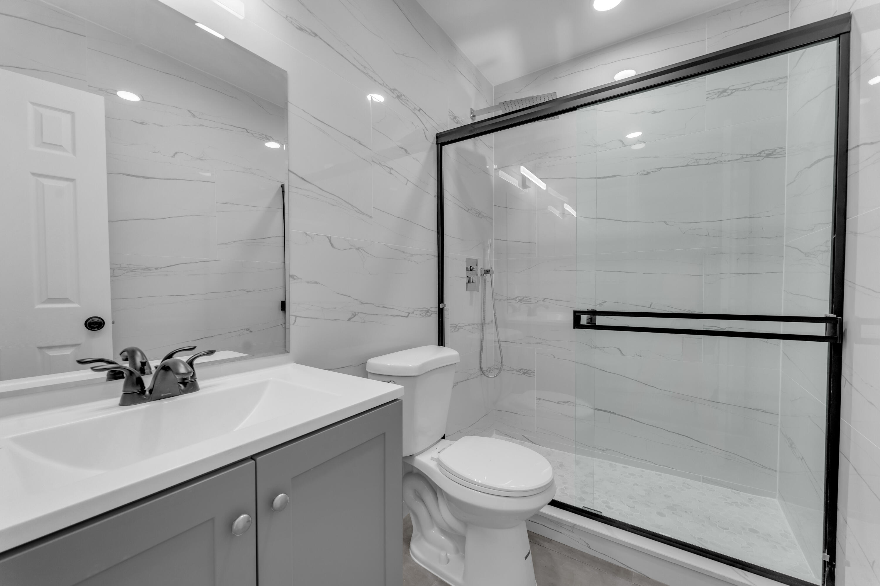Bathroom with a black-framed glass shower, marble-look tile, vanity, and toilet.
