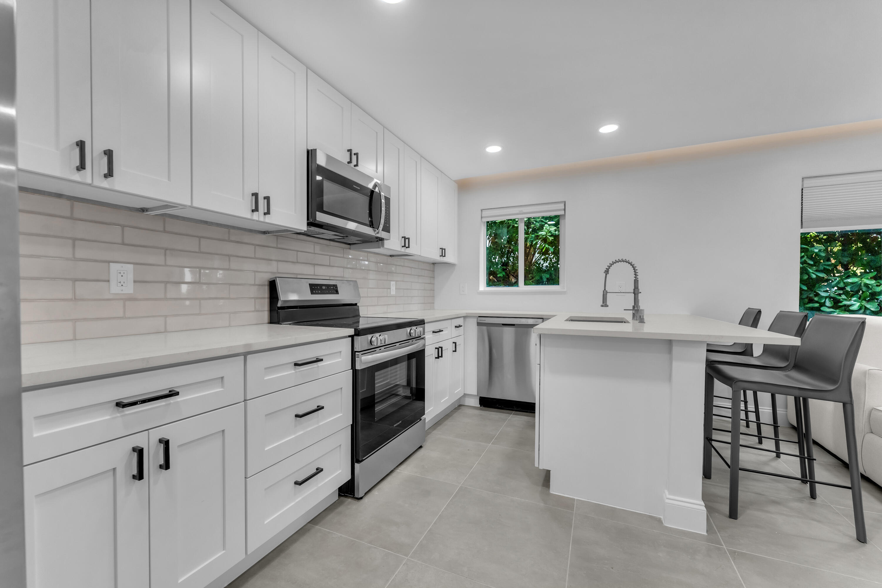 Renovated white kitchen with stainless appliances, subway tile backsplash, and island with gray bar stools.