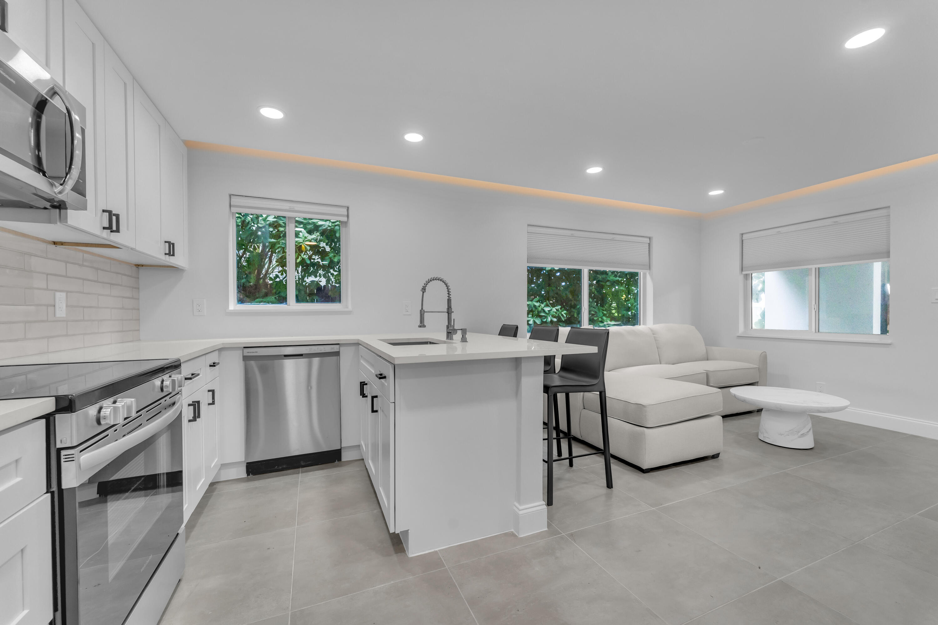 Open-plan kitchen and living room with a large island, stainless steel appliances, and white sectional sofa.