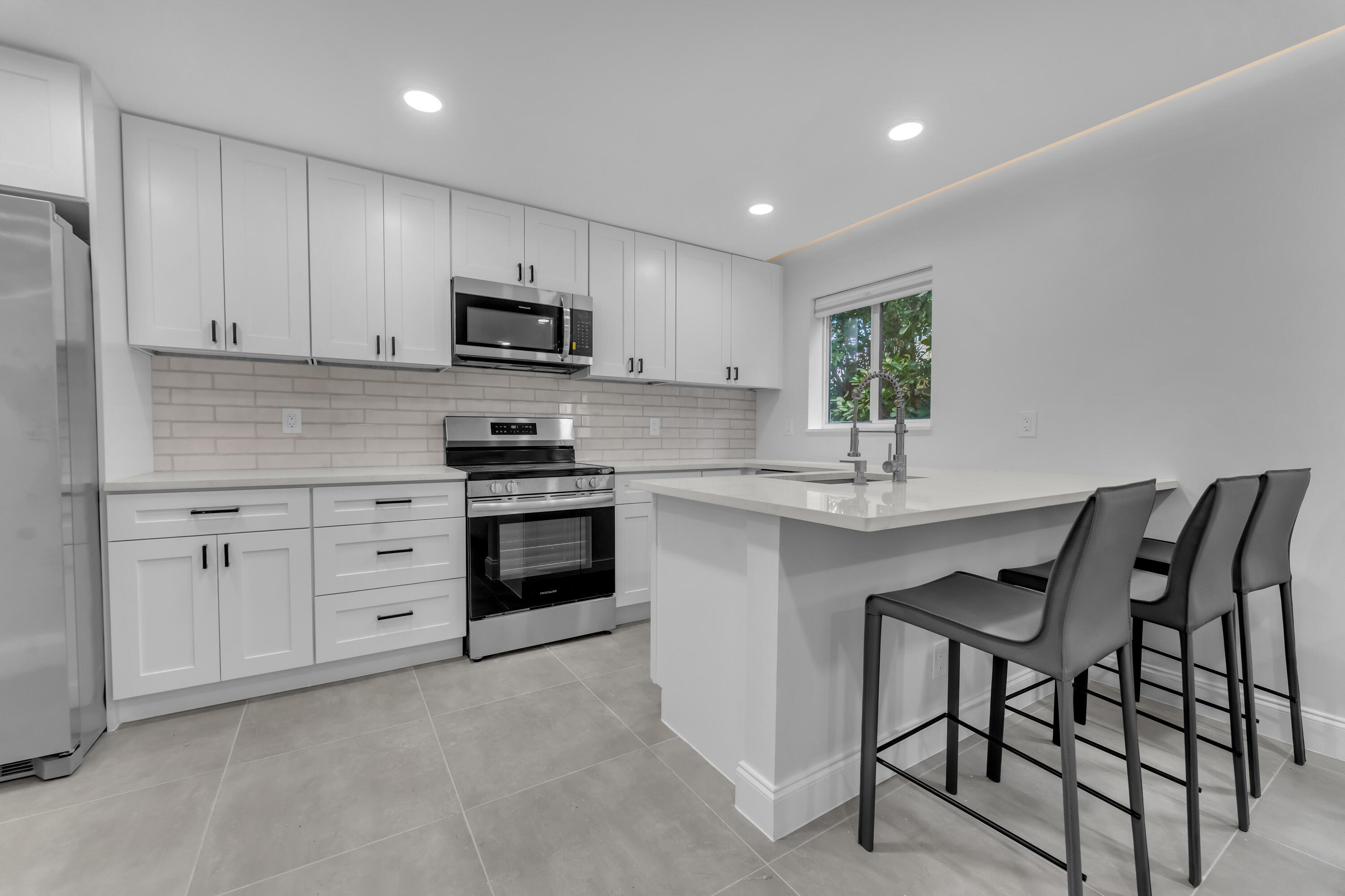 Renovated kitchen with white shaker cabinets, stainless steel appliances, and an island with three bar stools.