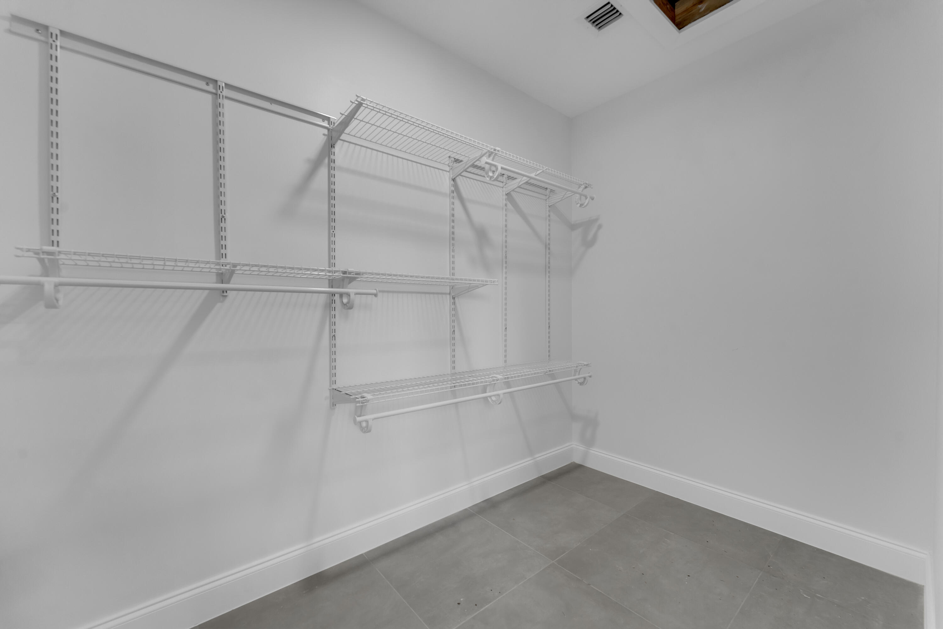 Empty walk-in closet with extensive white wire shelving and gray tile flooring.
