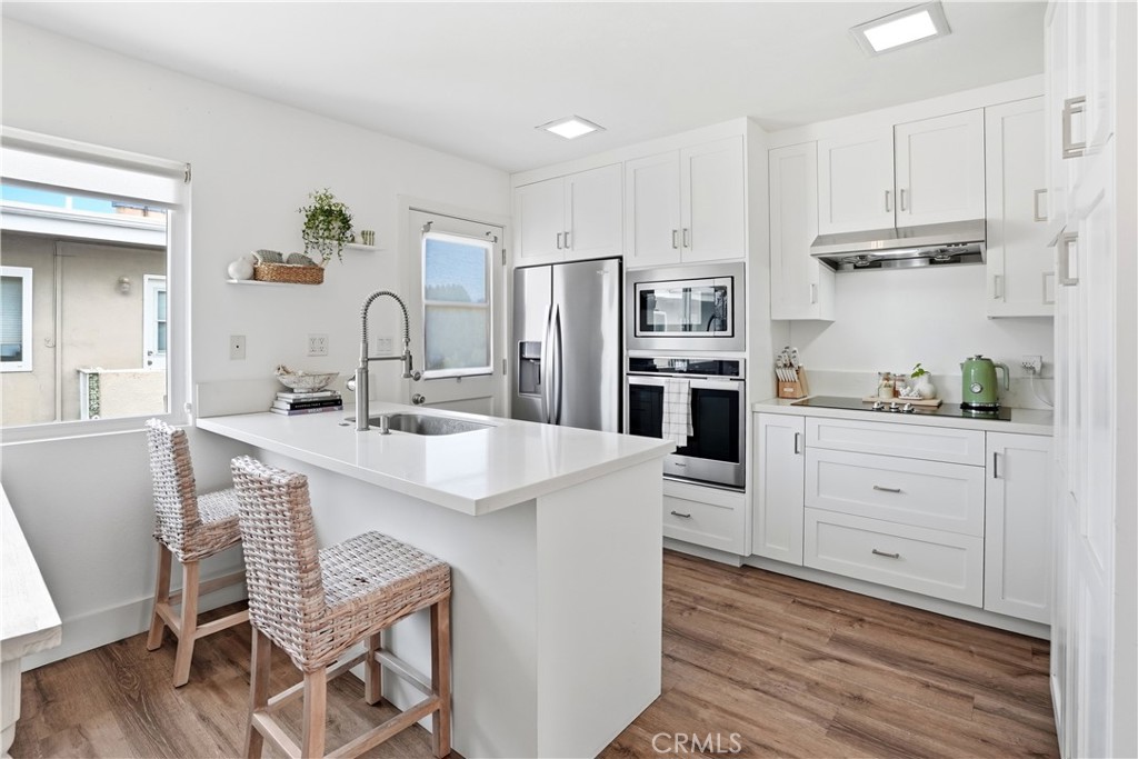 Bright white kitchen with a large island, stainless steel appliances, and woven bar stools.