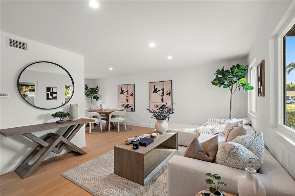 Staged living room and dining area with a round wall mirror and large windows.