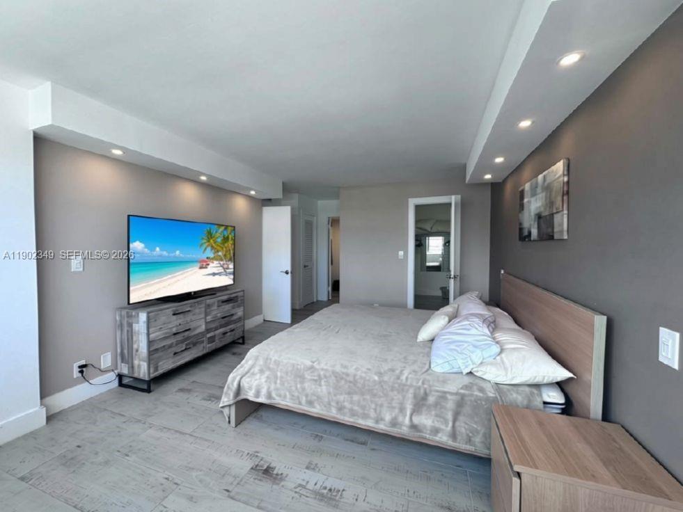 Furnished bedroom with a large bed, beach scene on the TV, and gray dresser.
