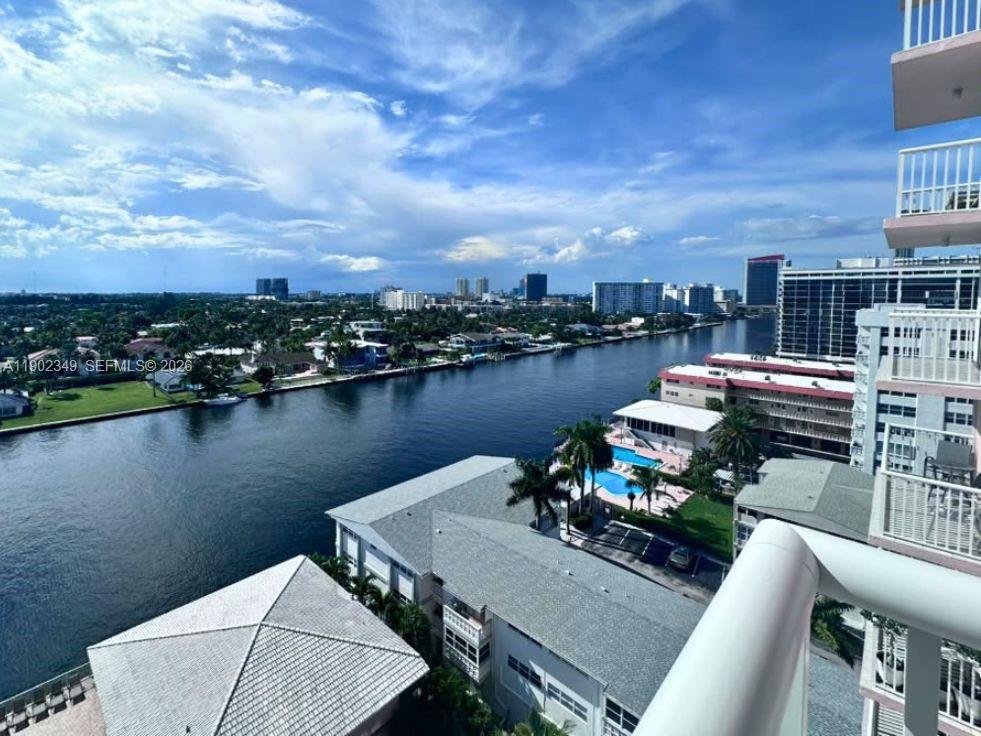Condominium waterway view toward a tree-lined neighborhood and distant city buildings, with a pool below.
