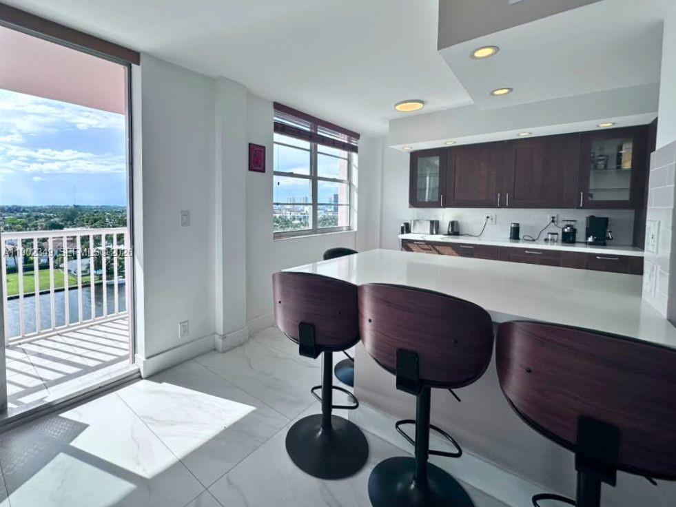 Modern kitchen with a white island and dark wood stools beside a balcony overlooking water.