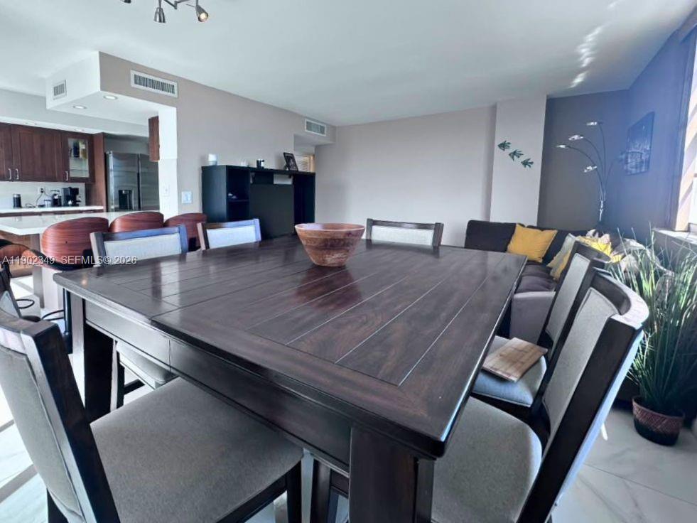 Dining area with a large dark wood table and gray chairs beside an open kitchen.