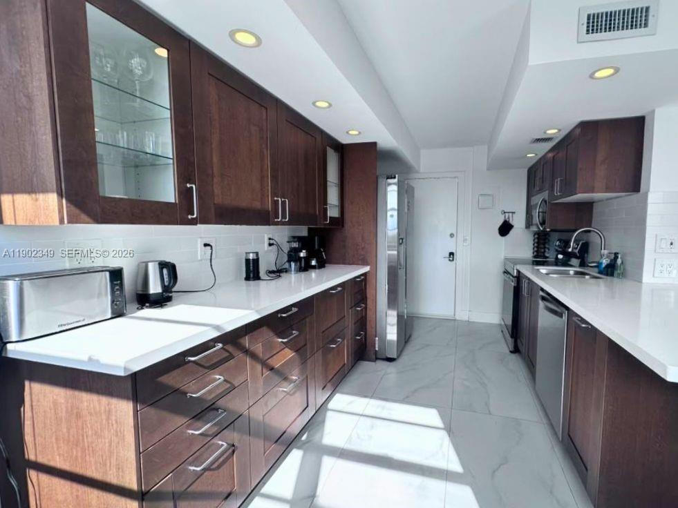Galley kitchen with dark wood cabinets, white countertops, and stainless steel appliances.