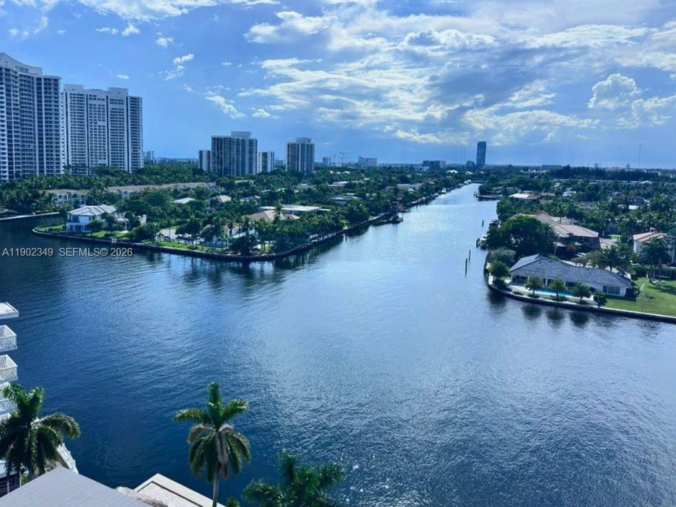 Aerial canal view bordered by waterfront homes and palm trees, with high-rise buildings in the distance.