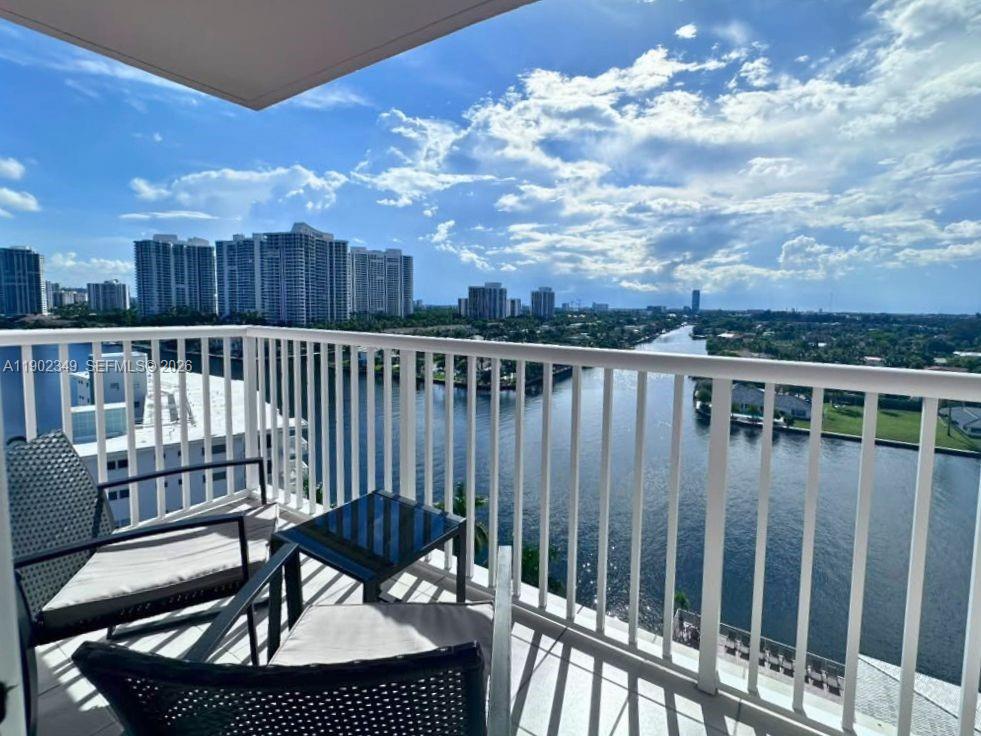 Furnished balcony overlooking a waterway and distant high-rise buildings.