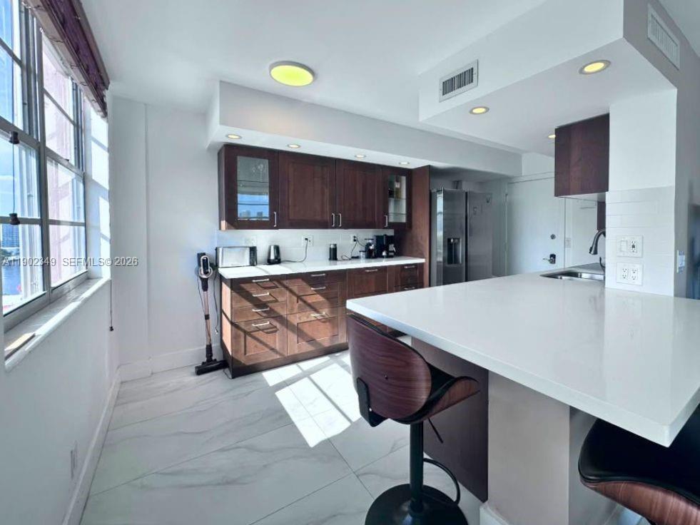 Modern kitchen with dark wood cabinets, stainless steel appliances, and a sunlit white breakfast peninsula.