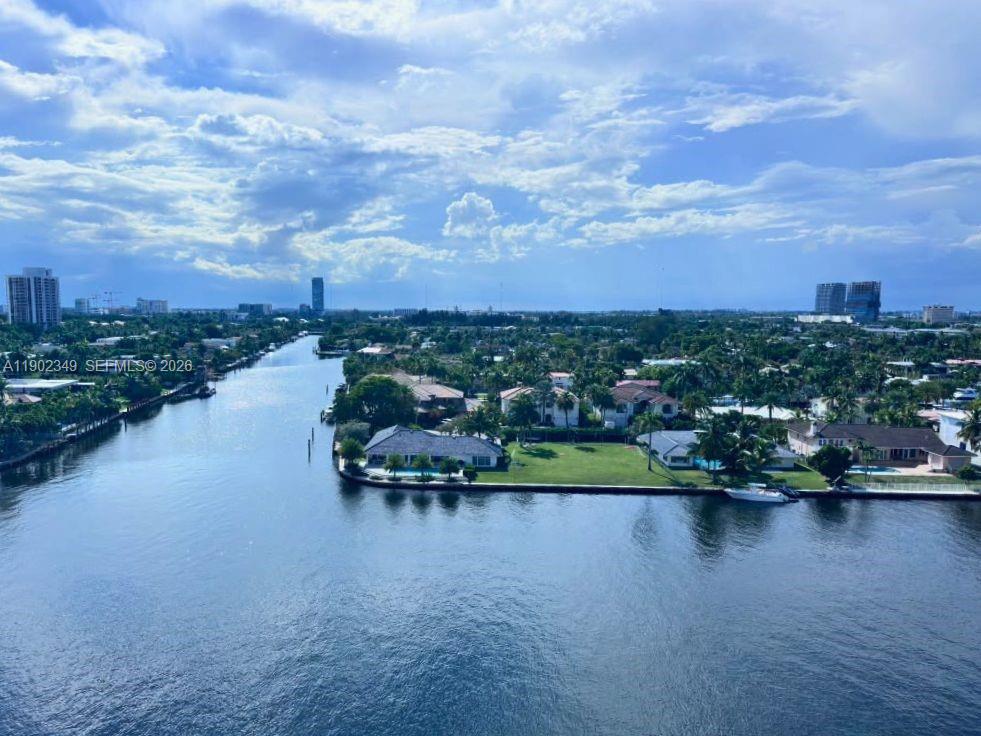 Aerial view over a canal and waterfront homes toward a distant skyline.