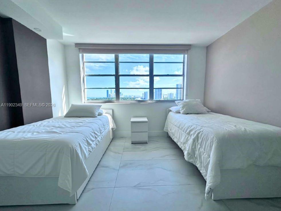 Bedroom with two white beds and a large window overlooking the city skyline.