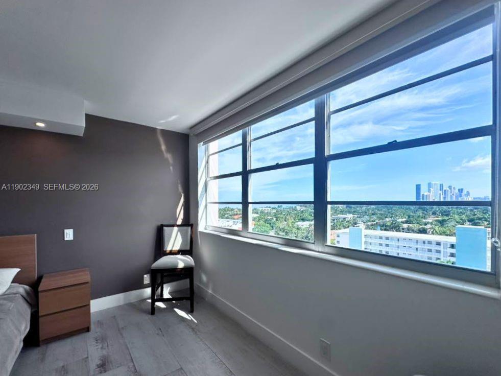 Bedroom with a wide window overlooking greenery and a distant city skyline.