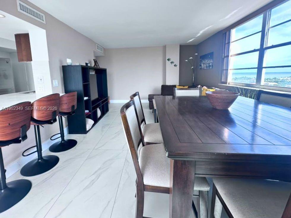 Condo dining area with a dark wood table, breakfast bar, and broad windows overlooking the coast.