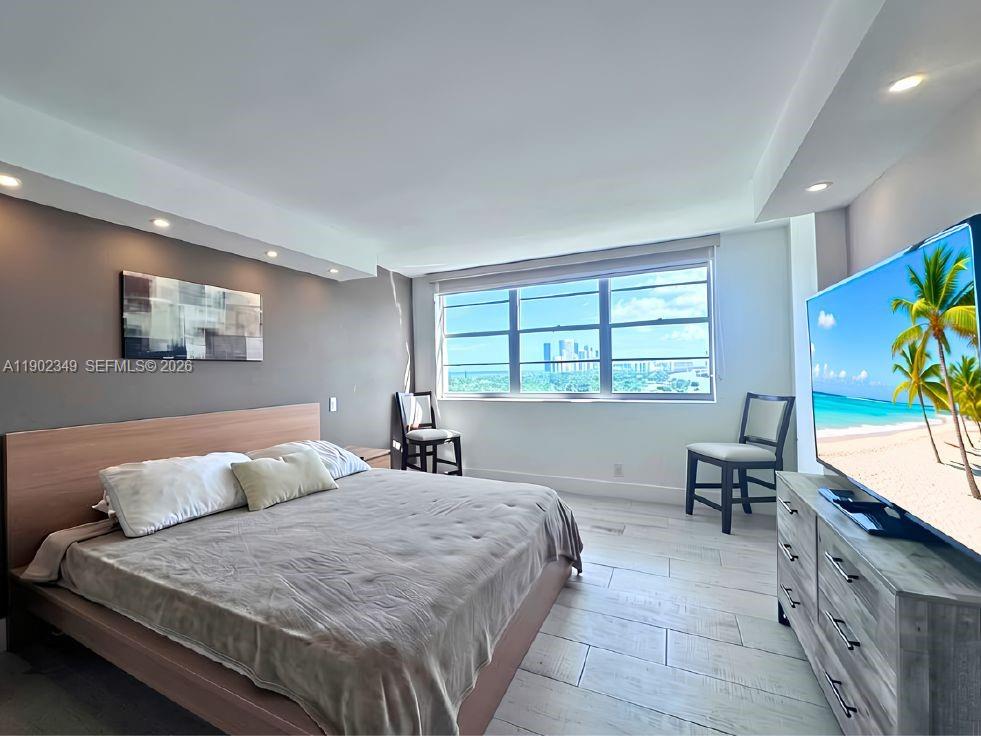 Furnished bedroom with a large bed, gray walls, and a window overlooking distant buildings.