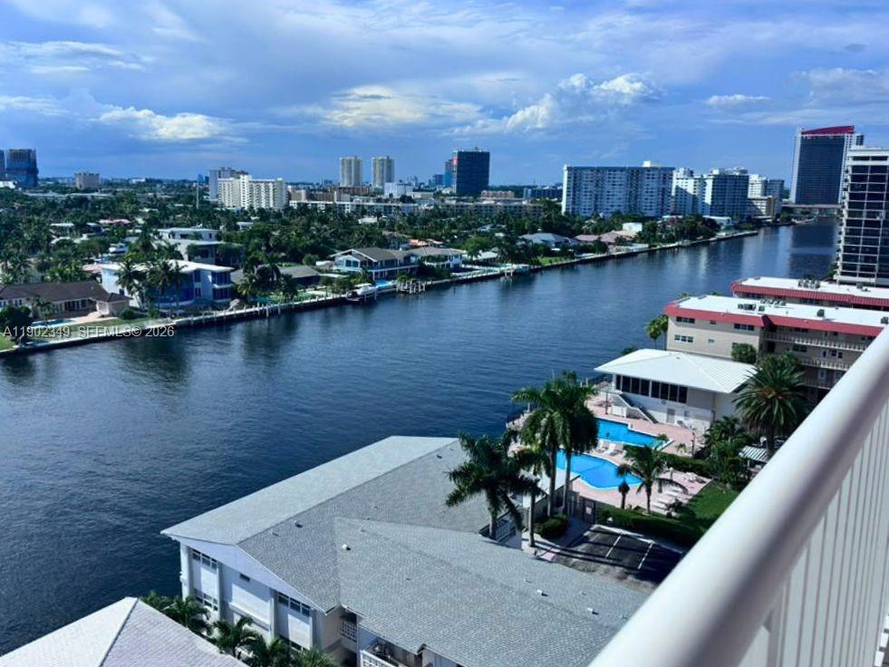 Canal and waterfront homes seen from a balcony, with a pool and distant city skyline.