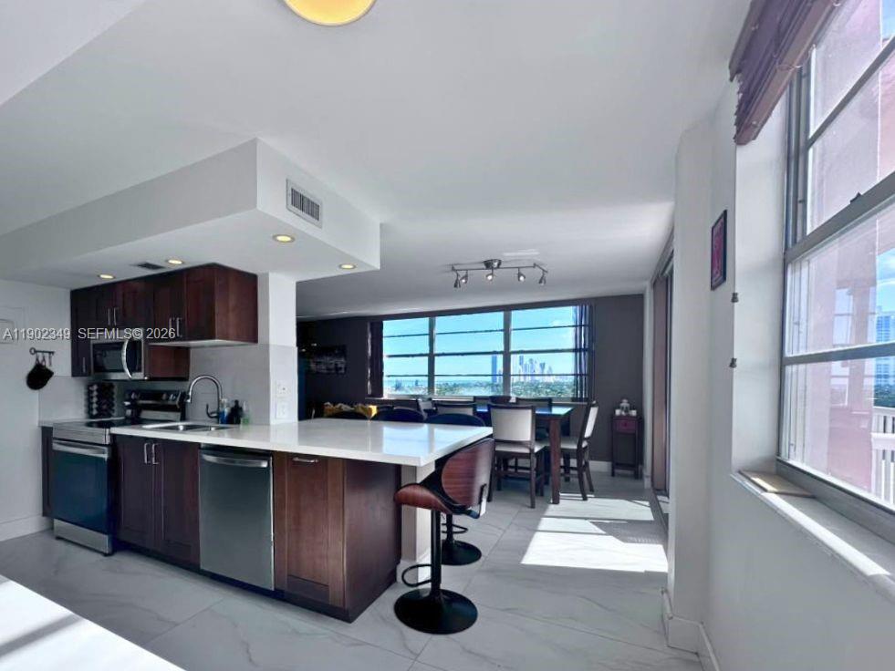Open-plan condo kitchen with a white breakfast bar and large windows overlooking water and a distant skyline.
