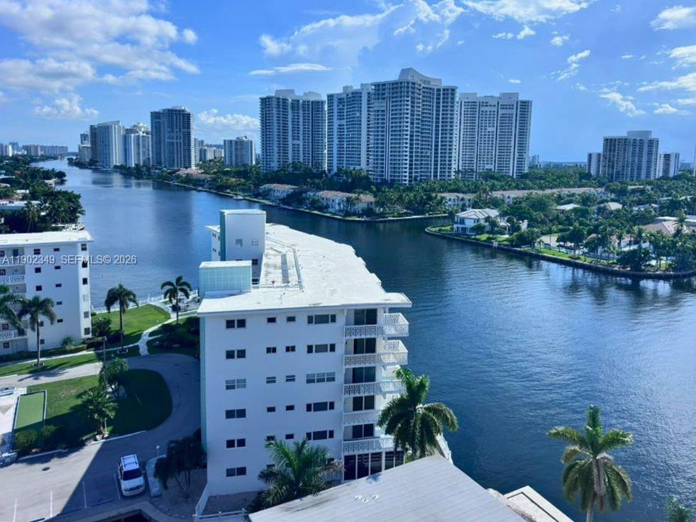 Waterfront high-rises line a canal beside a white condominium building and palm trees.