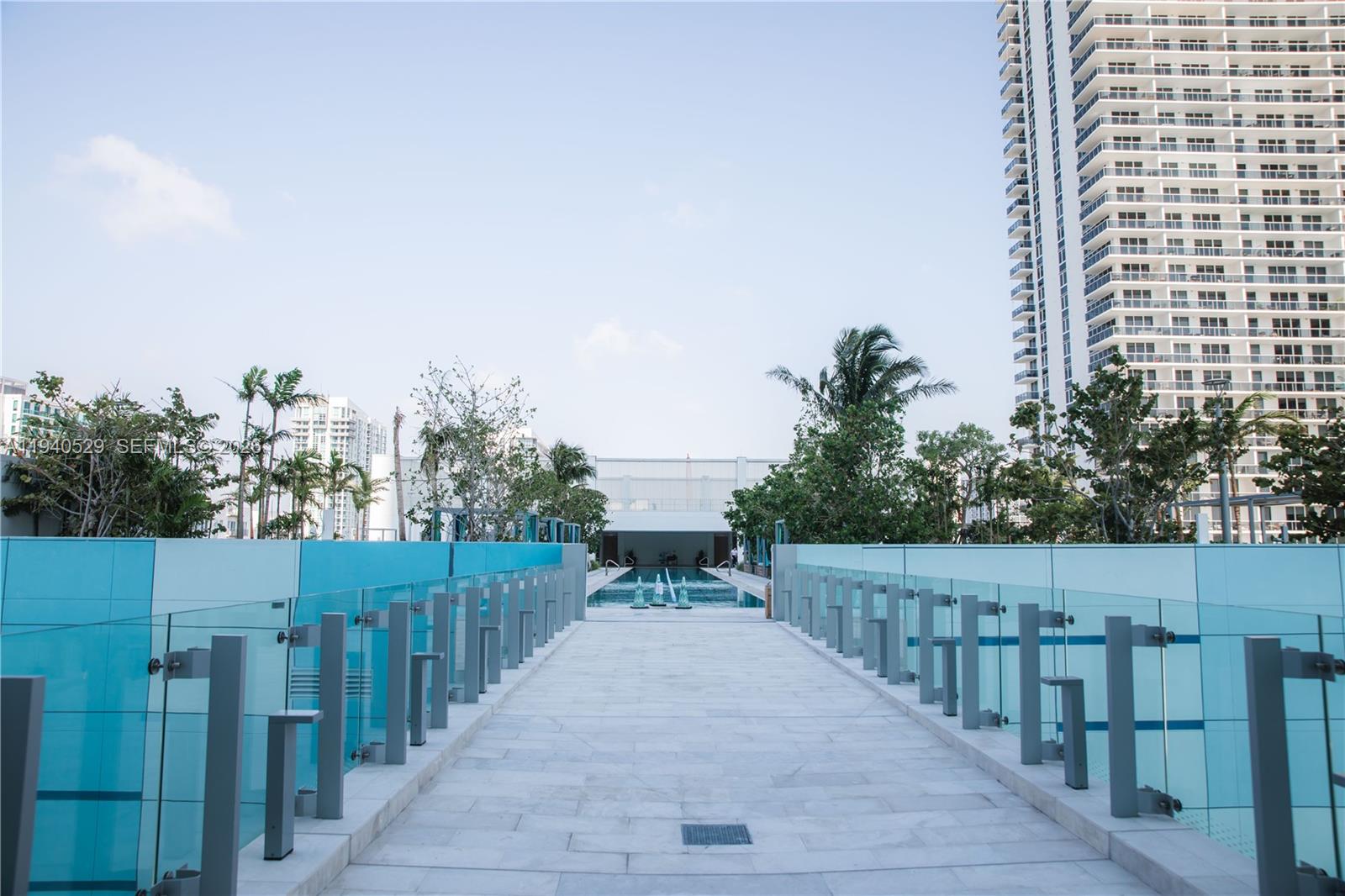 High-rise pool deck with turquoise glass railings, palm trees, and a walkway leading to the pool.