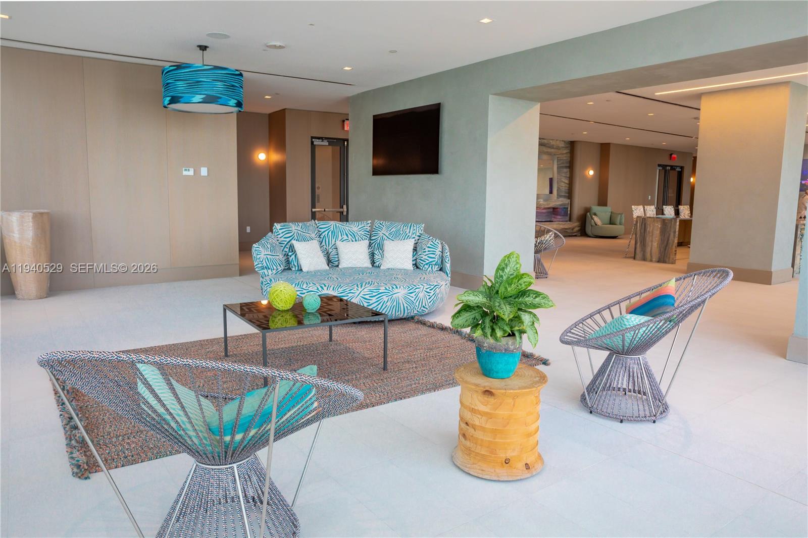 Condominium lounge with turquoise patterned seating, woven chairs, and a potted plant.