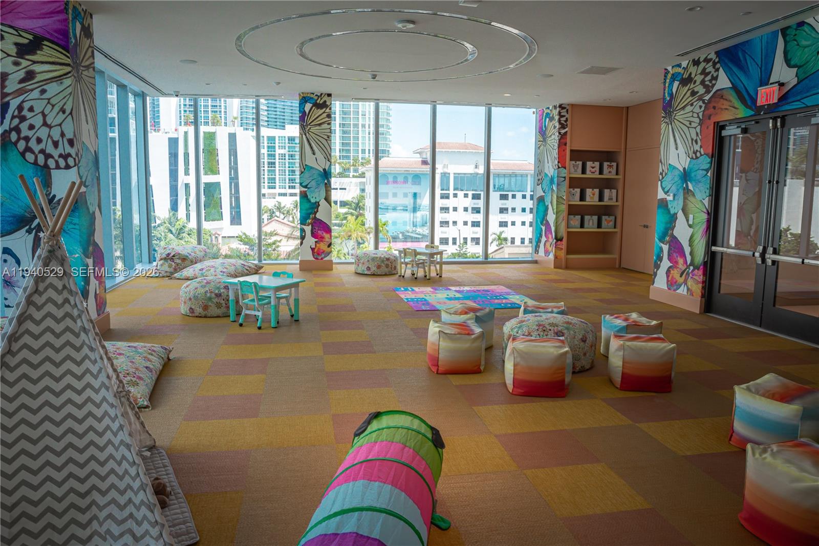 Children’s playroom with butterfly murals, colorful seating, and large windows overlooking nearby buildings.