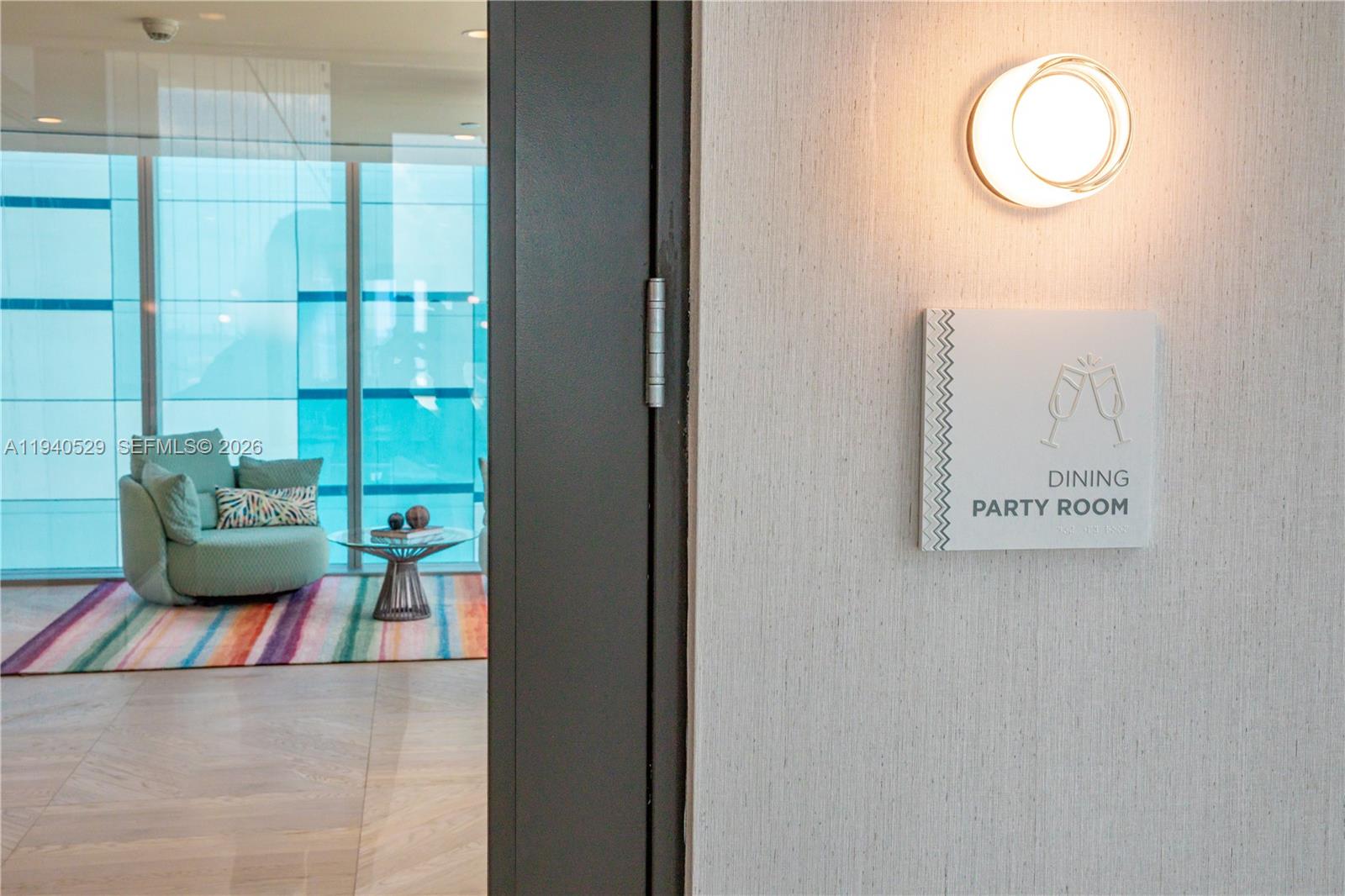 Dining party room entrance with a wall sign, lounge chair, and colorful striped rug.
