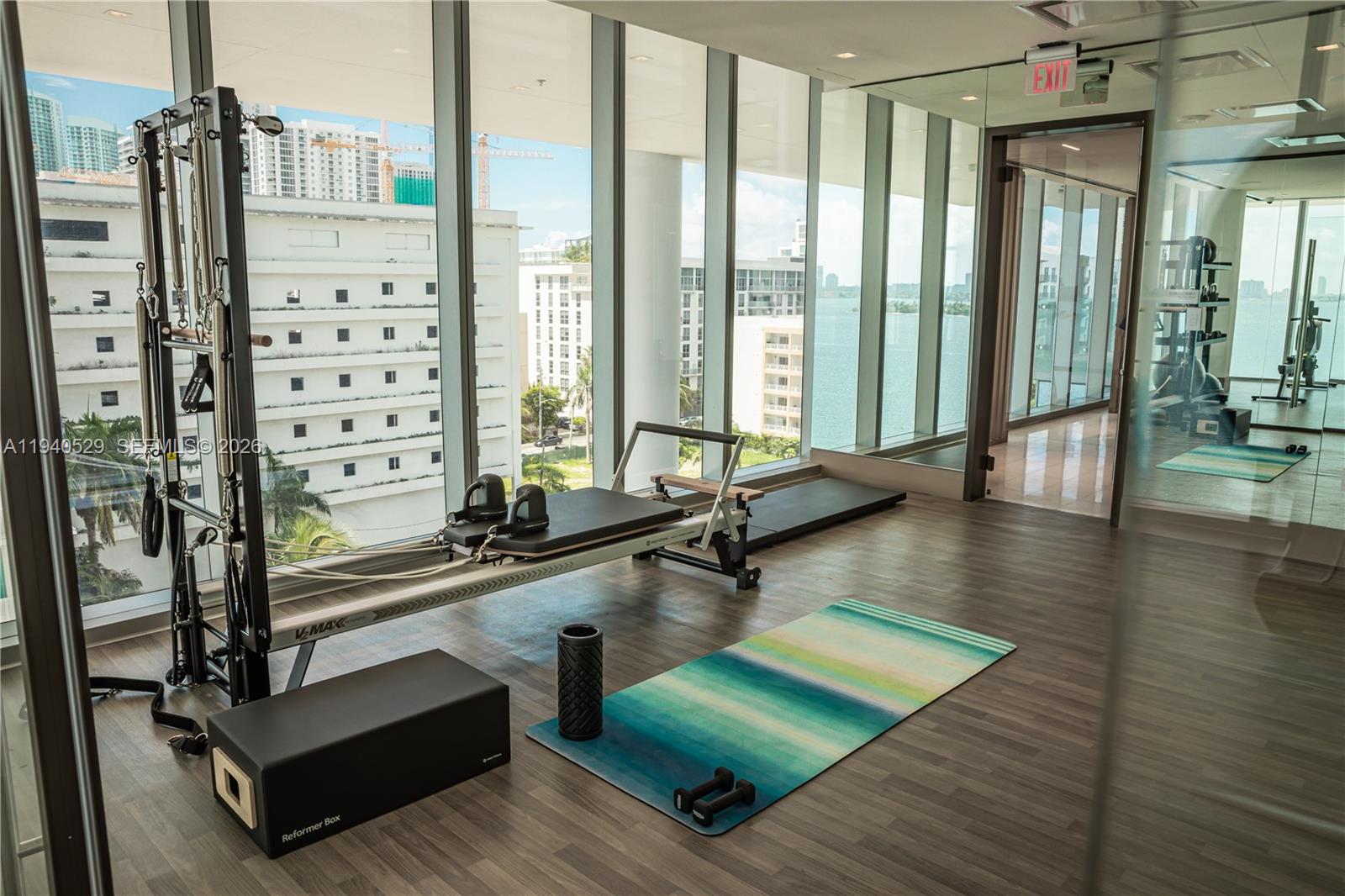 Fitness room with Pilates reformers and a yoga mat beside windows overlooking Biscayne Bay.