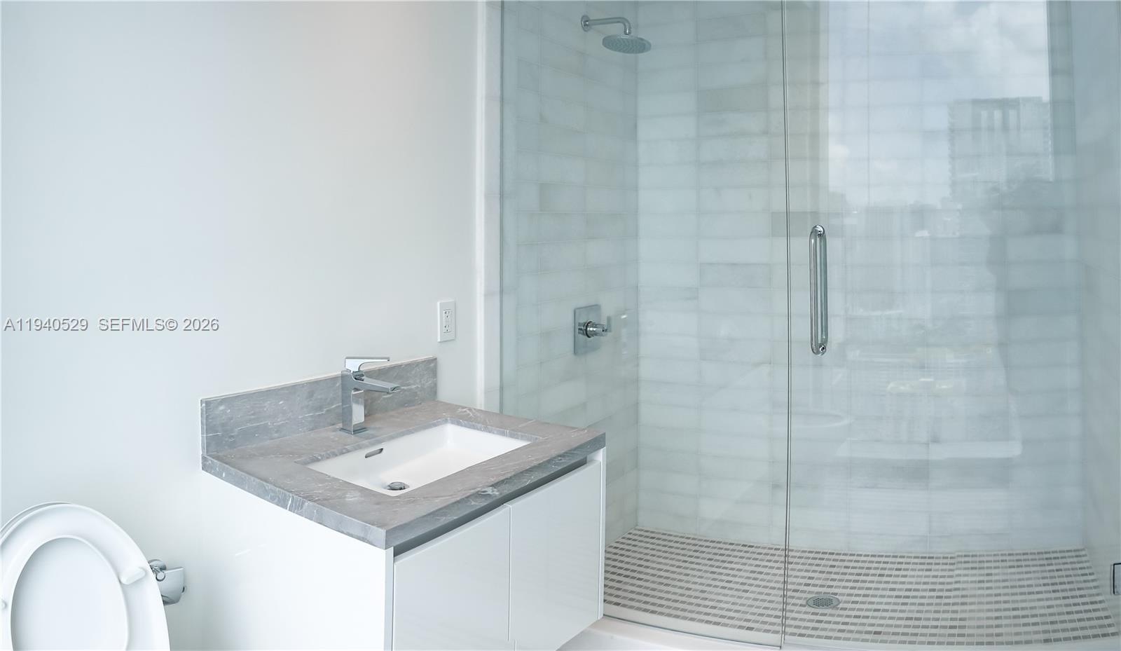 Modern bathroom with a gray stone vanity and glass-enclosed tiled shower.
