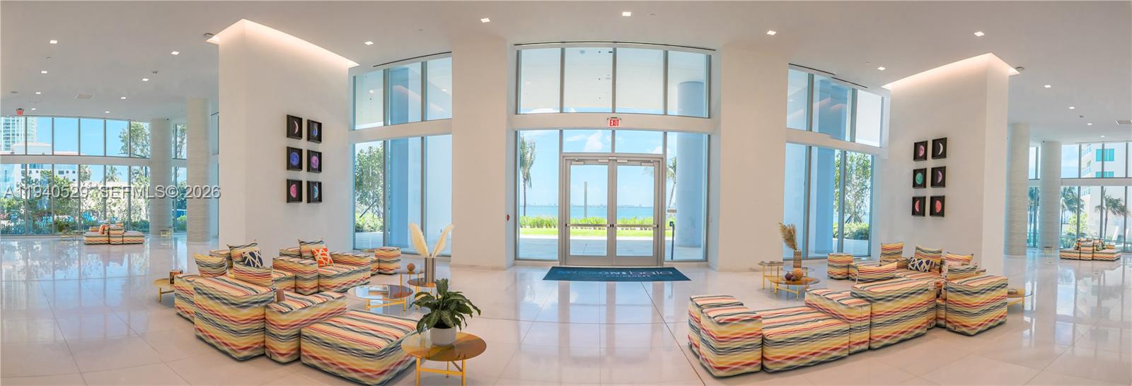 Bright condominium lobby with colorful lounge seating and ocean views through floor-to-ceiling windows.