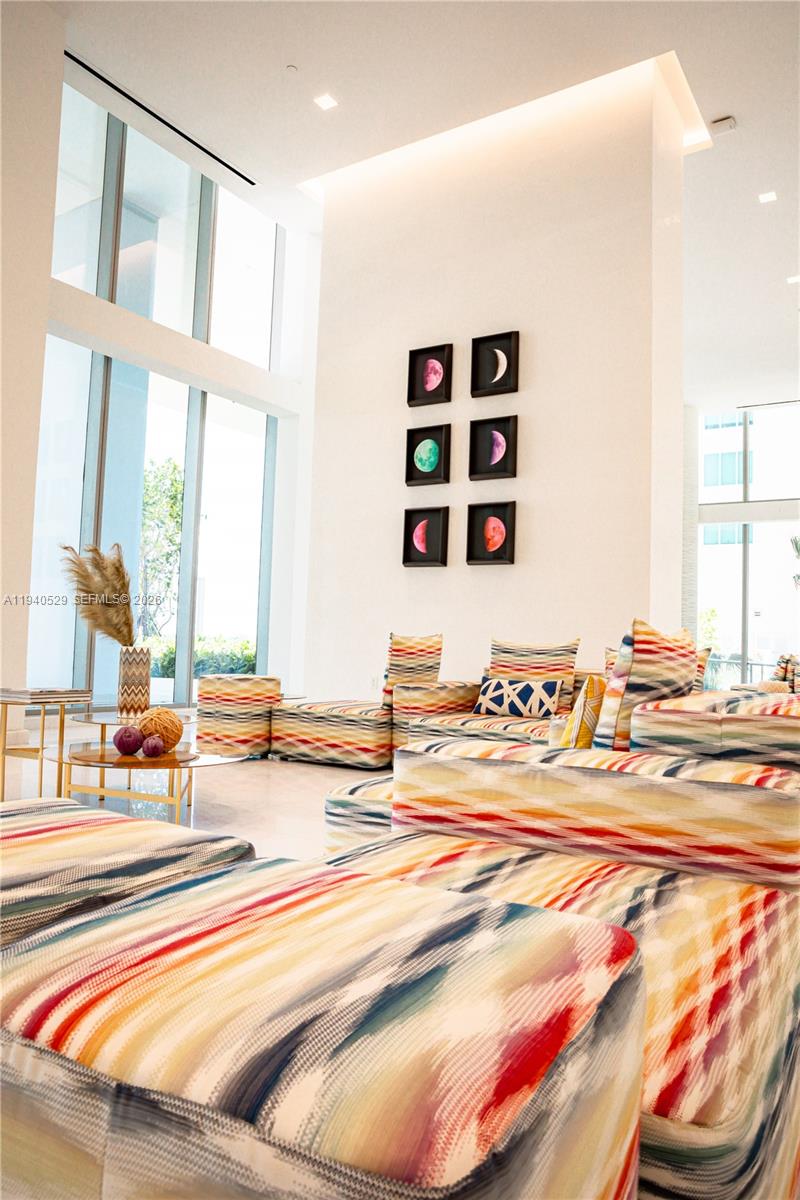 Bright double-height lounge with colorful patterned sofas and framed moon-phase artwork.