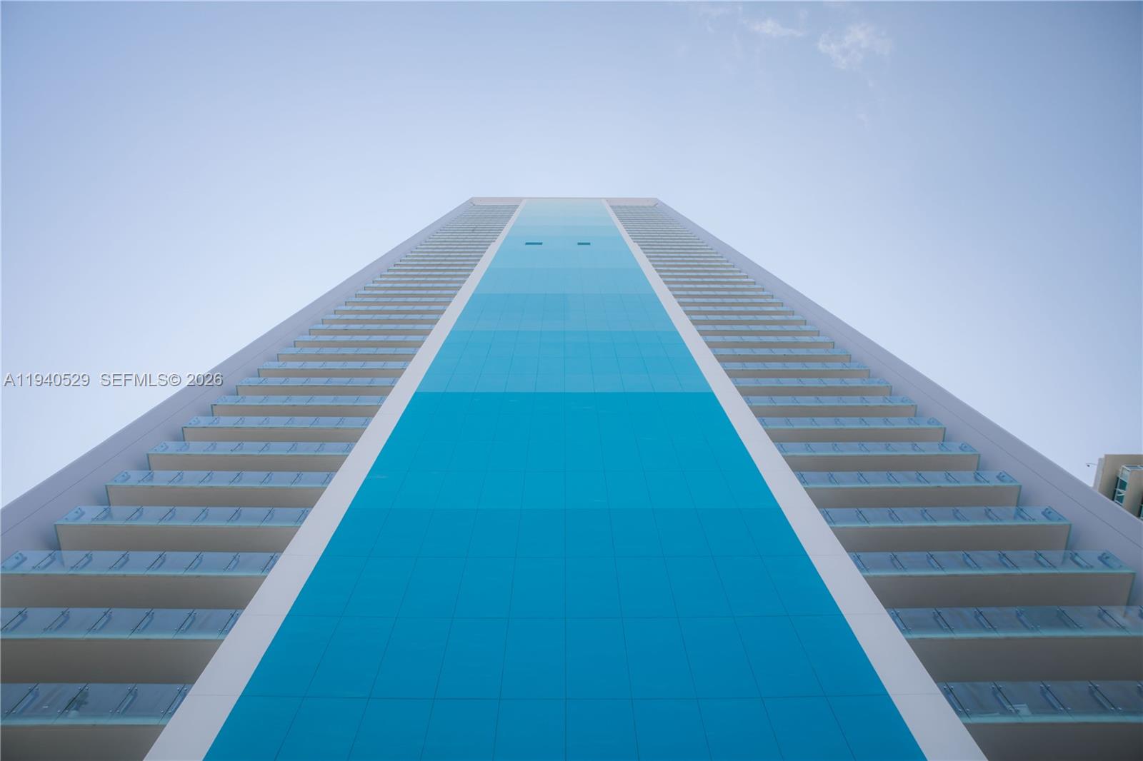 Modern high-rise facade with a vivid blue glass center strip and rows of balconies, viewed from below.