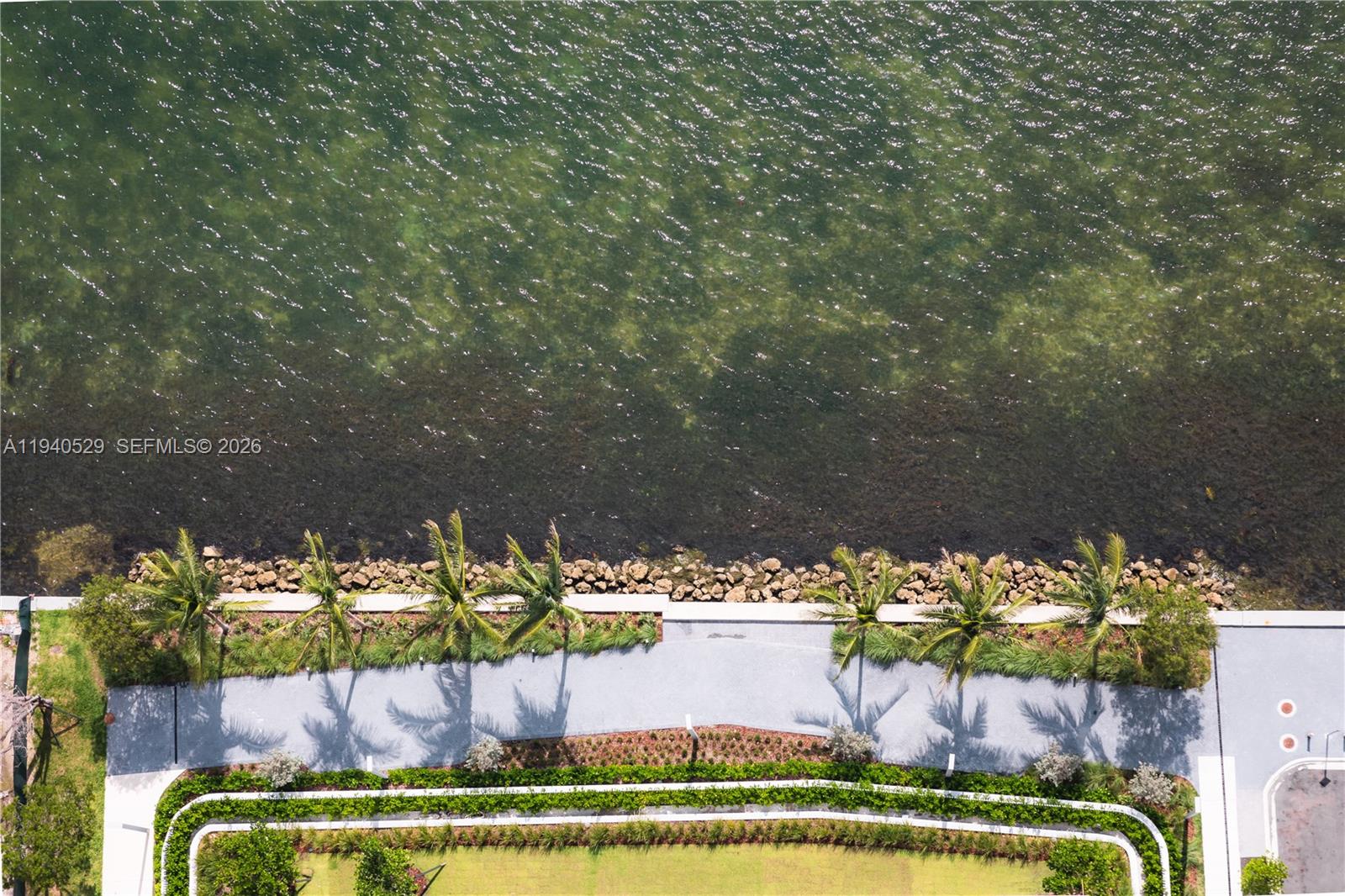 Aerial waterfront view with a rocky shoreline, palms, and landscaped paths.