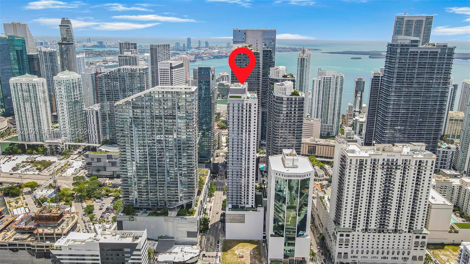Aerial view of downtown Miami towers and Biscayne Bay, with a red pin marking a waterfront building.
