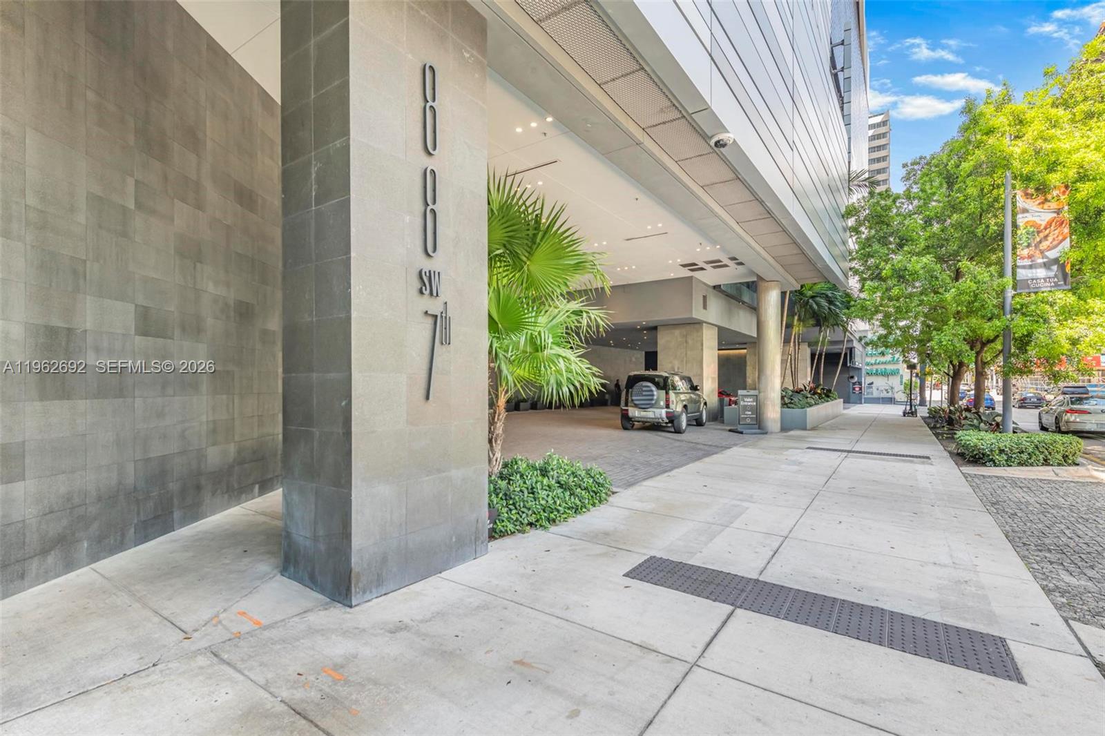 High-rise entrance at 88 SW 7th Street, with a covered driveway, stone facade, and landscaped sidewalk.