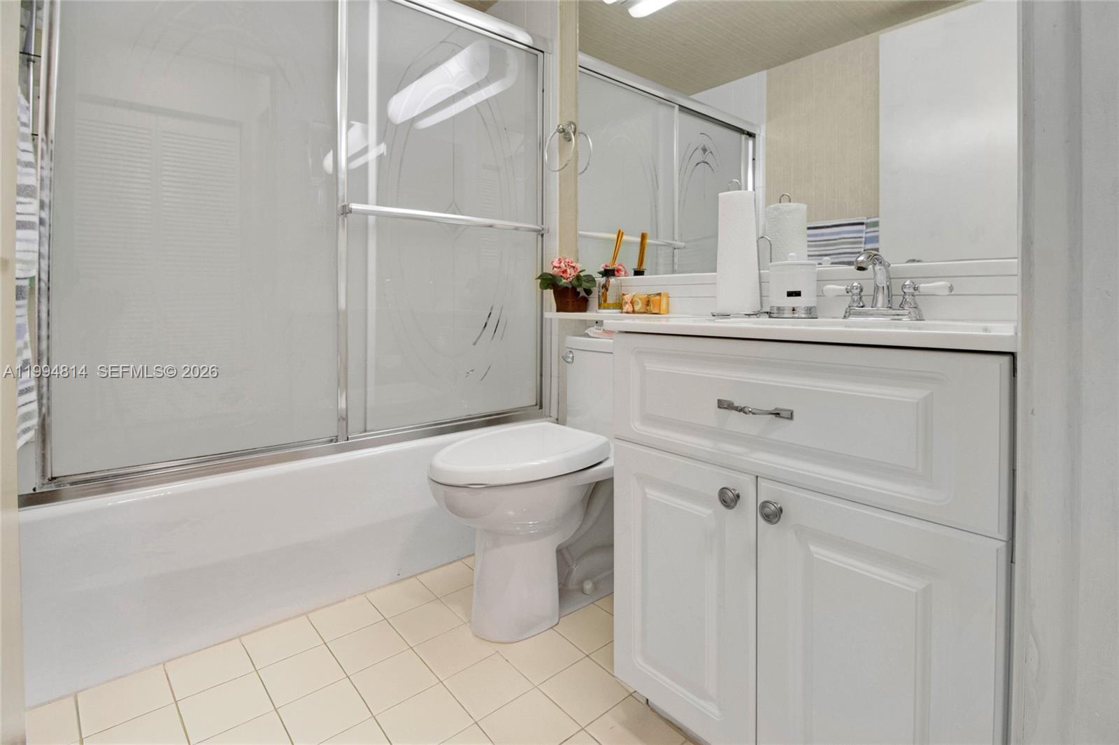 Bathroom with a glass-enclosed bathtub, toilet, and white vanity with chrome fixtures.