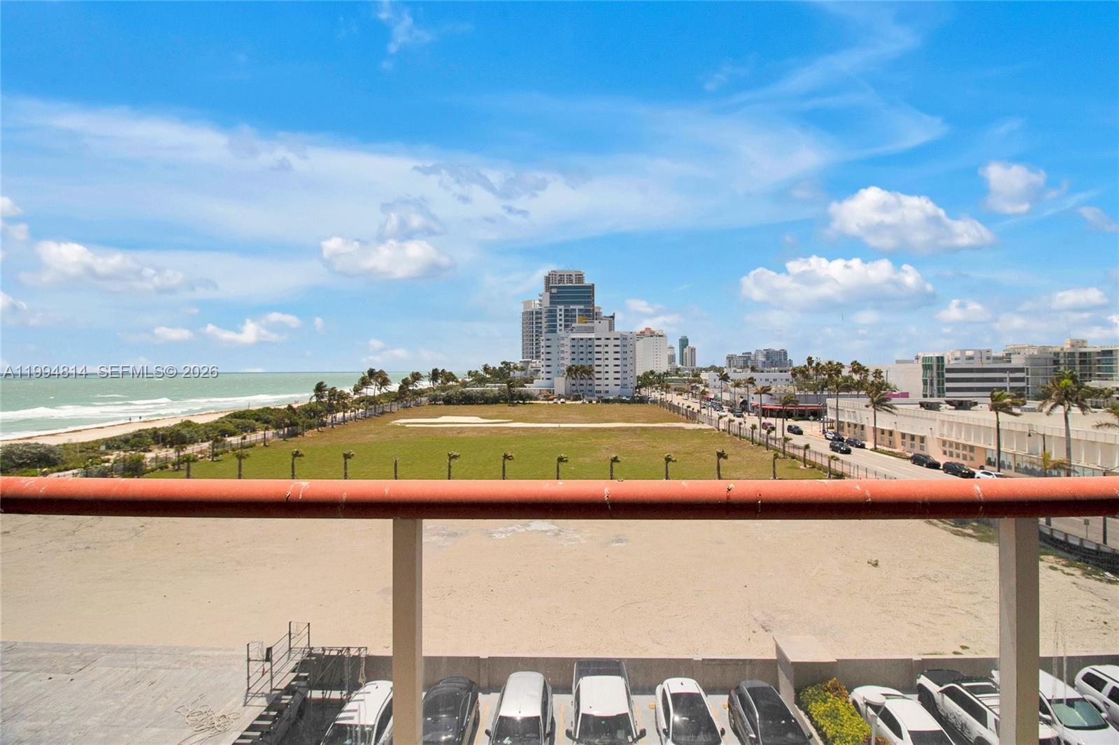 Balcony view overlooking a sandy beach, ocean, and coastal buildings.
