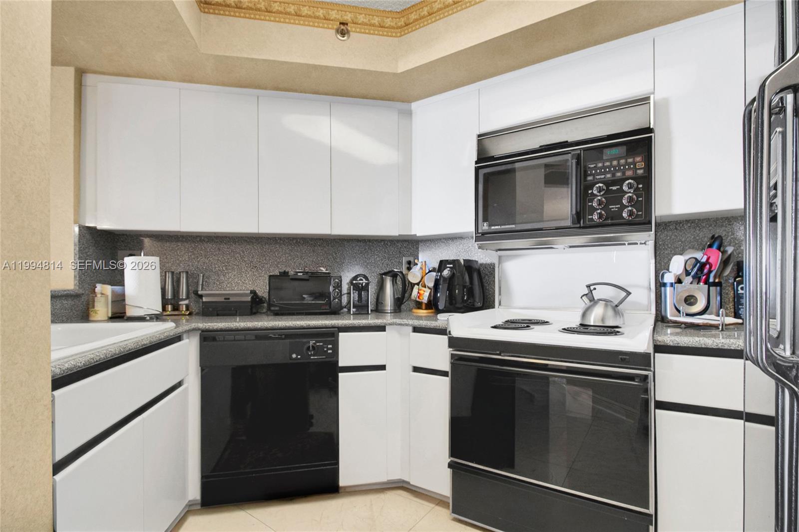 Kitchen with white cabinets, speckled gray counters, and a black-and-white range with microwave.