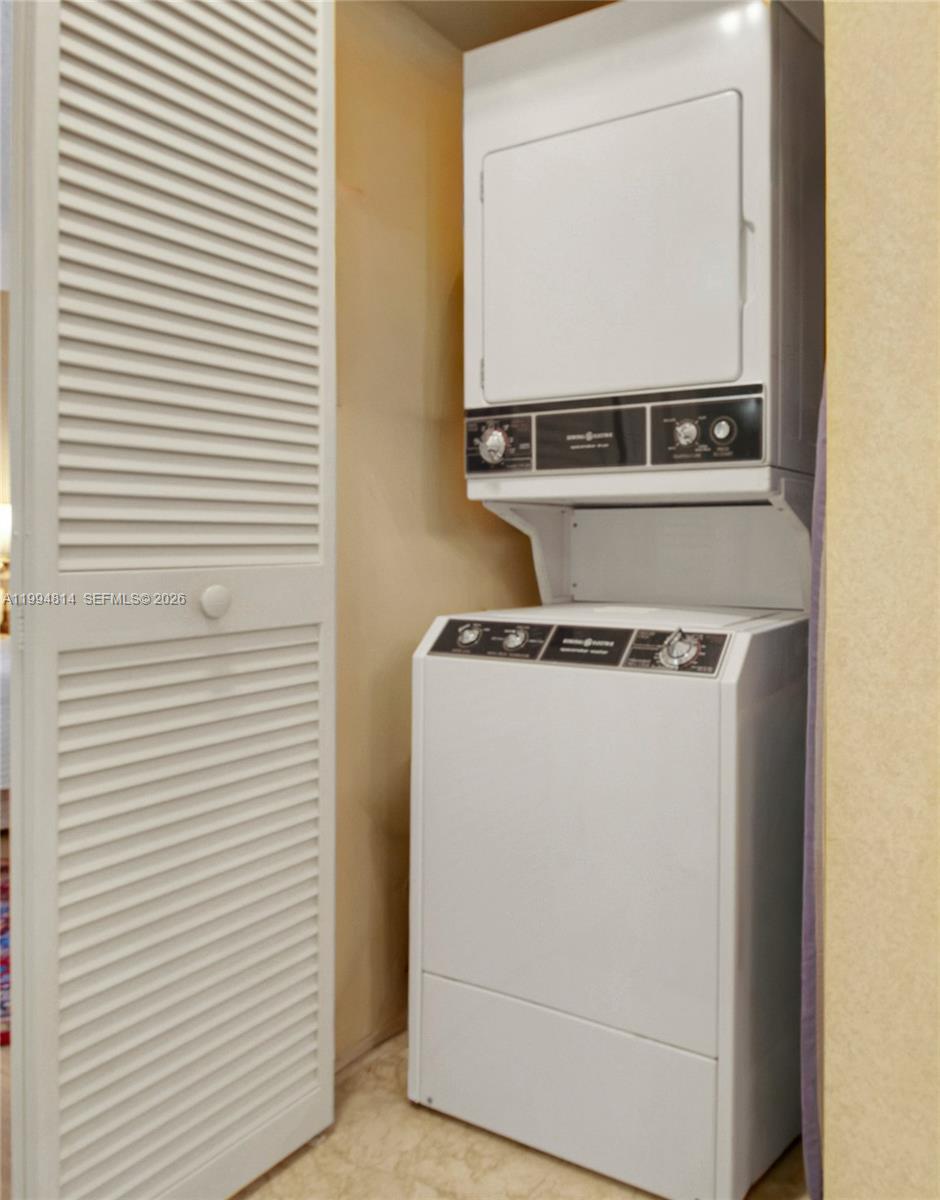 Stacked washer and dryer in a narrow closet beside a white louvered door.