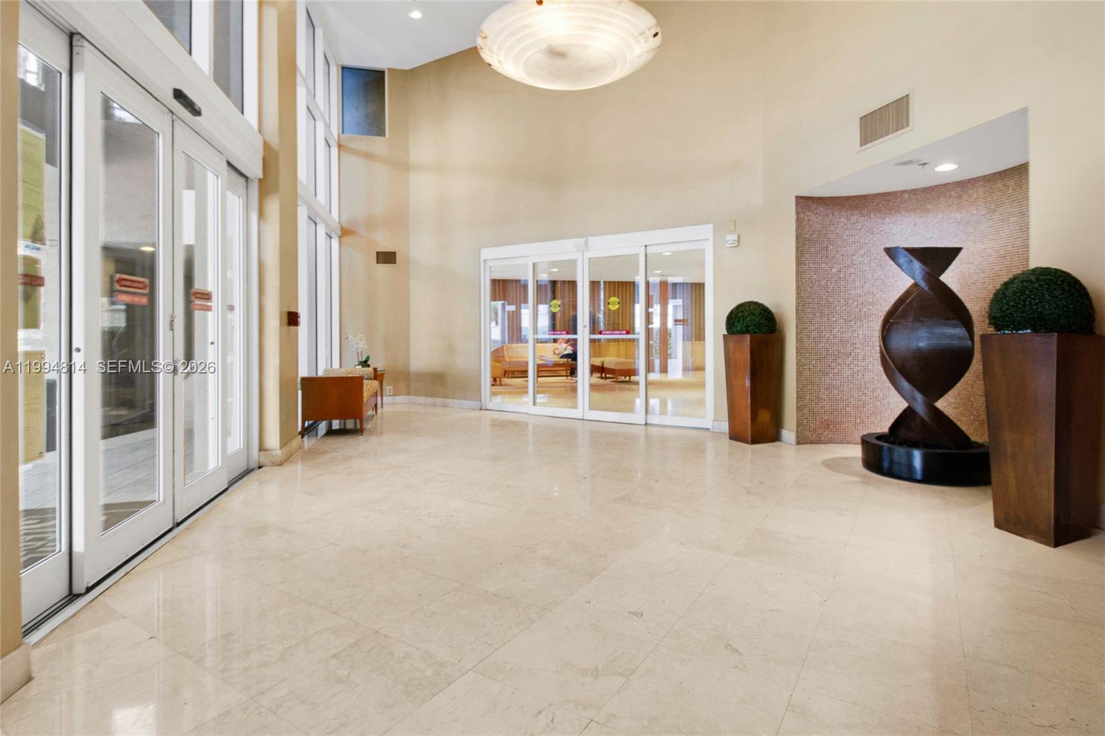 Condominium lobby with polished marble floors, tall glass doors, and a dark abstract sculpture.