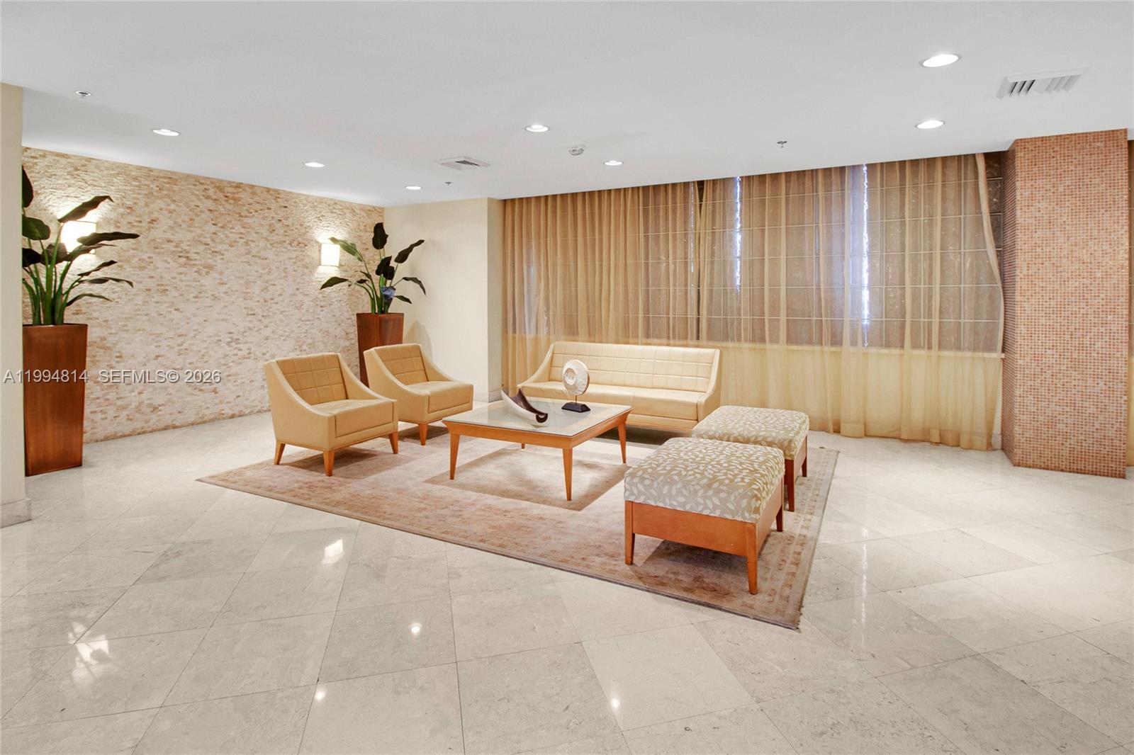 Condominium lobby lounge with cream seating, a stone accent wall, tall curtains, and potted plants.