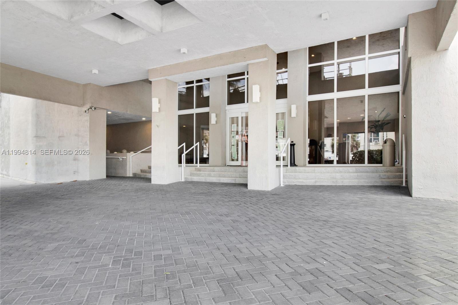 Condominium entrance with a covered drop-off, glass facade, and paved forecourt.