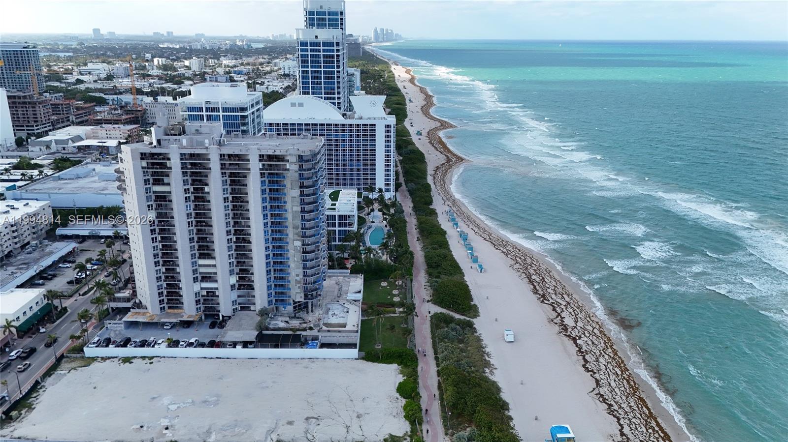 Beachfront condominium towers beside a sandy shoreline and turquoise ocean.