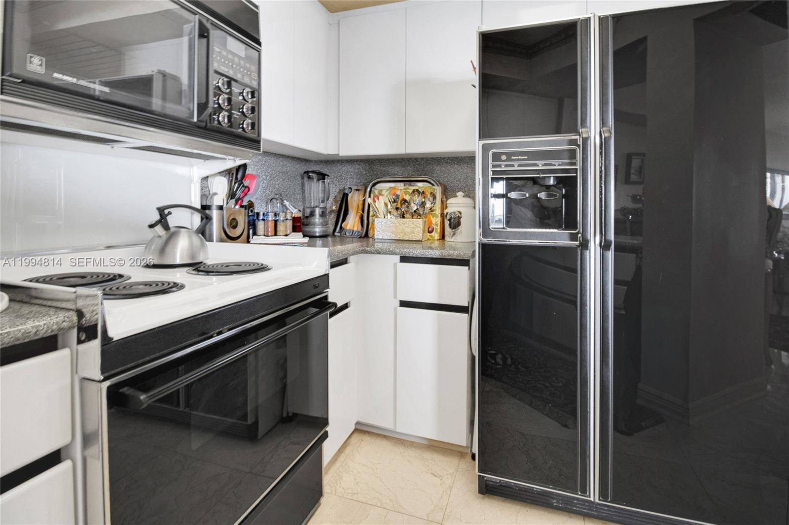 Kitchen with white cabinetry, electric range, microwave, and dark side-by-side refrigerator.